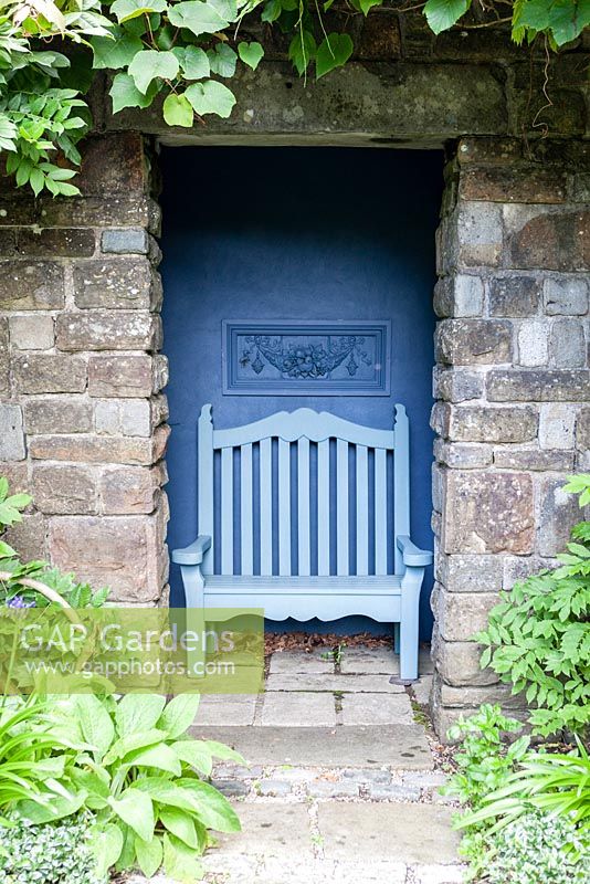Blue painted wooden seat in stone shelter with blue painted interior wall. The Ridler Garden, Swansea, South Wales. July. Designed and created by Tony Ridler