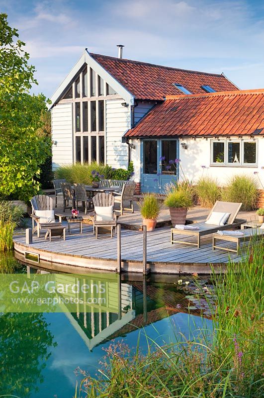 Tranquil summer scene of the house, outside seating area and swimming pond. 