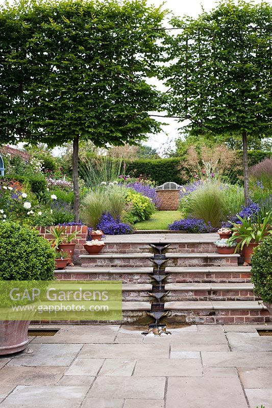 Contemporary country garden with steps incorporating water rill to upper level with herbaceous borders