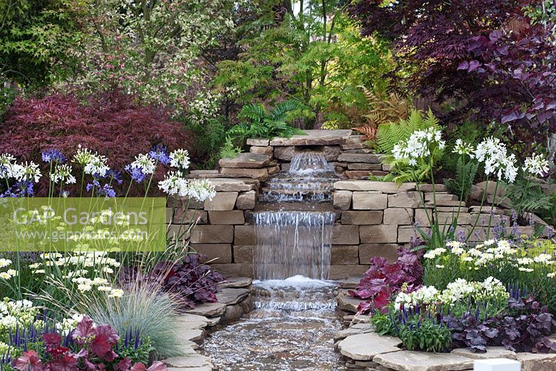 The waterfall in the centre of 'The Water Garden' at RHS Tatton Flower Show 2015, bordered by dense, colourful planting 