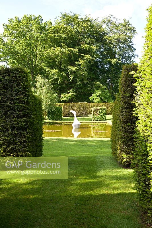 Clipped Yew hedges lead to a contemporary Japanese pond garden. White marble sculpture 'Hokusai's boat' by Jessica Walters. Designer Georgia Langton. Farleigh House, Hampshire.