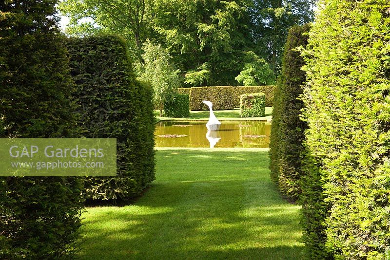 Clipped Yew hedges lead to a contemporary Japanese pond garden. White marble sculpture 'Hokusai's boat' by Jessica Walters. Designer Georgia Langton. Farleigh House, Hampshire.