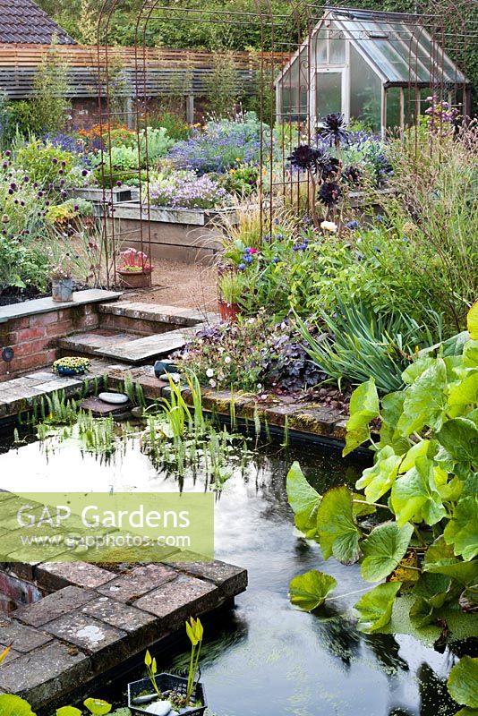 Sunken patio with raised pond and beds of perennials and herbs. The Coach House