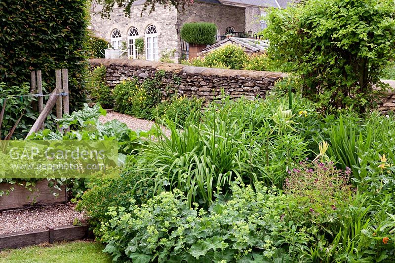Head of the border with vegetable garden behind the stone wall, with rosemary grown in the old chimney pots from the house. Fawley House, North Cave, Yorkshire, UK. 
