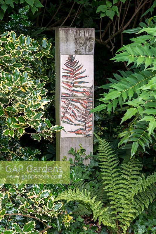 Painted ceramic tiles with a fern pattern on a wooden post in a shady corner.