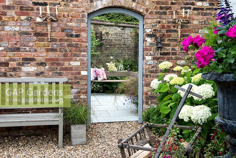 Seen past front urn of pelargoniums and salvias and Hydrangea 'Annabelle', doorway frames view of small courtyard garden