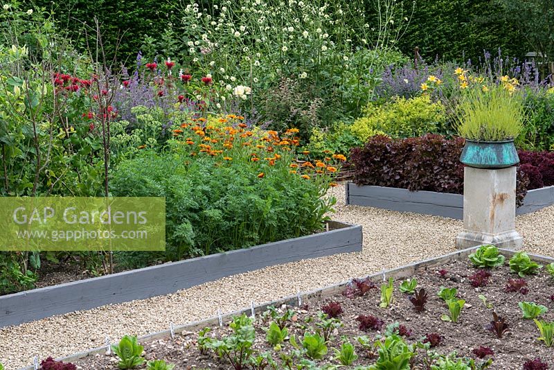 A potager with raised beds of vegetables and flowers including chives, salad leaves, peas, marigolds, bergamot and daylilies.A stone plith with a copper pot of lavender provides a focal point.