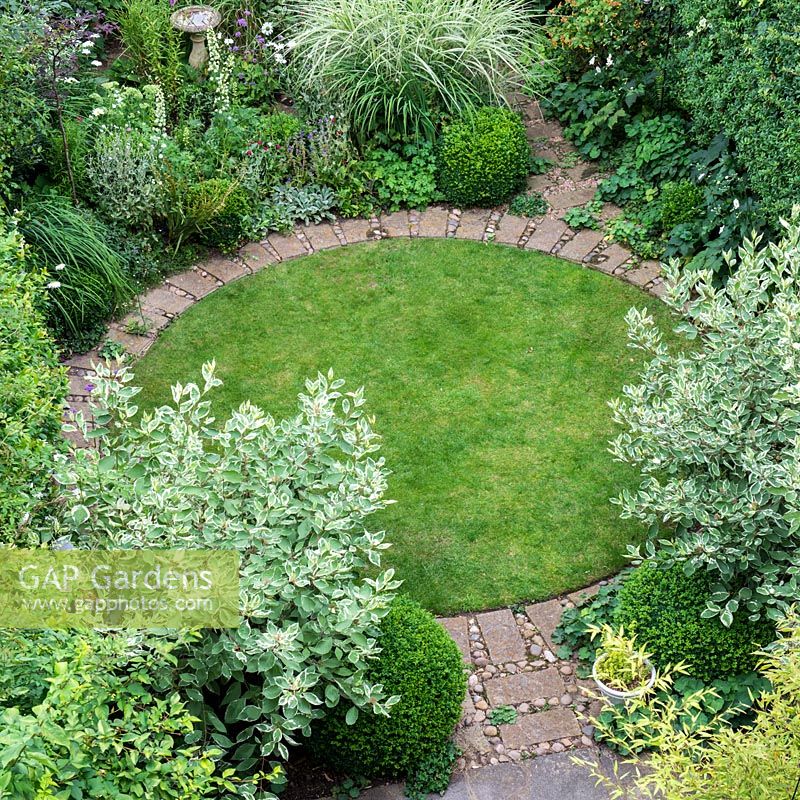 An aerial view of a circular lawn surrounded by a brick path, Cornus alba 'Elegantissima', Miscanthus grass and Buxus sempervirens balls.