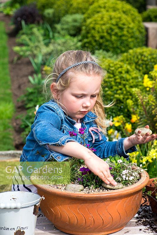 Young girl planting an alpine container garden. Add pebble decoration.