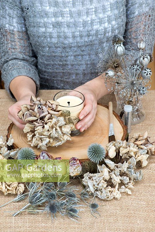 Creating a festive table decoration with garden flowers and seed heads. Glue hydrangea heads onto oak base, forming a skirt around the candle.
