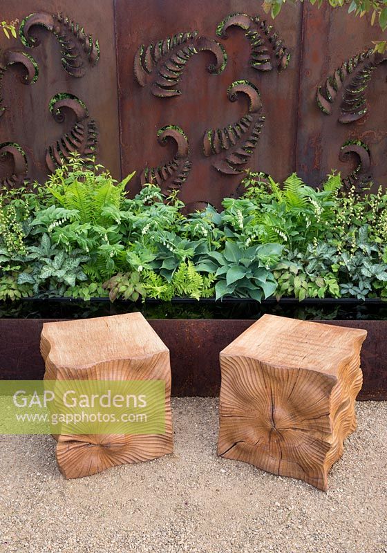 Two carved oak cube wooden seats on gravel path, rusted steel fern wall panel, reflective water feature, planting of ferns, hosta, Constraining Nature garden - designed by Kate Durr Garden Design - Best Festival Garden award and a gold medal - RHS Malvern spring festival 2015