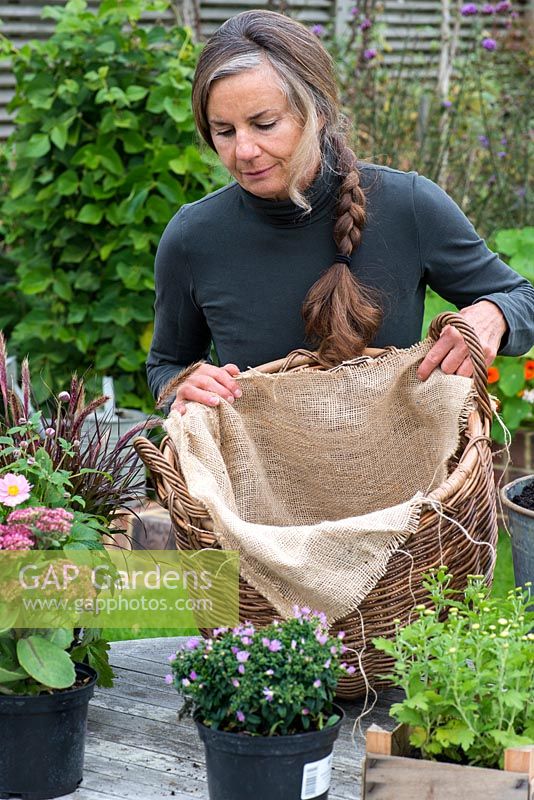 Planting a log basket with early autumn flowering perennials. Lining with sacking which will be visible through the loose weave of the basket, and hide the black plastic inner liner.