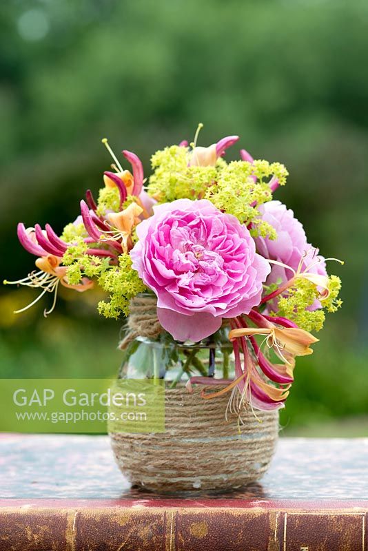 A colourful summer posie with pink rose, alchemilla and honeysuckle in a glass jar decorated with twine.