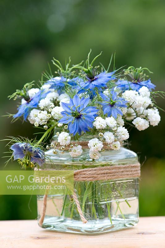 A summer posie of Nigella damascena - Love in the mist and baby's breath in a glass jar decorated with twine.