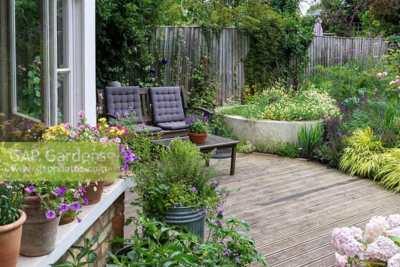 A small town garden with decked seating area surrounded by mixed borders and containers with herbs, flowers and vegetables.