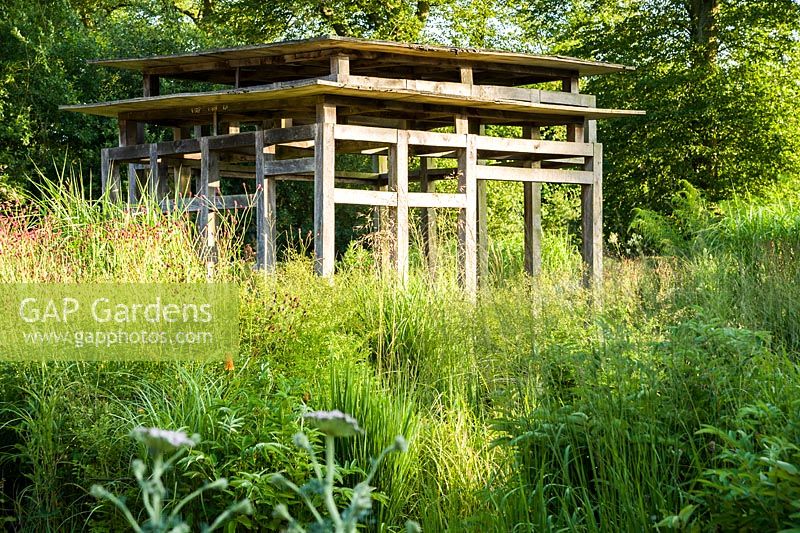 At the centre of the minimalist front garden, designed by Christopher Bradley-Hole, is a contemporary green oak summerhouse surrounded by tall miscanthus and other grasses mixed with herbaceous perennials including sanguisorbas. Bury Court Barn, Bentley, Hants, UK