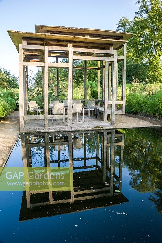 At the centre of the minimalist front garden, designed by Christopher Bradley-Hole, is a contemporary green oak summerhouse beside a still pool surrounded by tall miscanthus and other grasses. Bury Court Barn, Bentley, Hants, UK