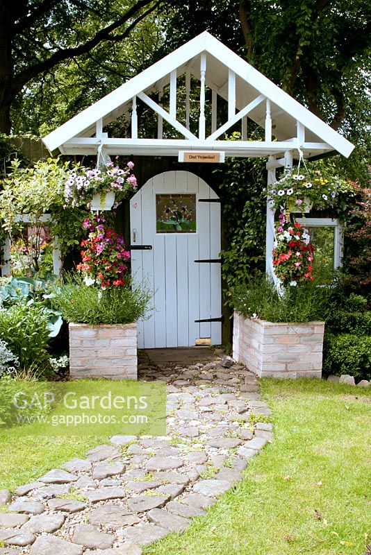 Lych gate in fence with side mirrors and hanging baskets in small back garden with raised beds and gravel and cobble path at 'Arevinti', Stubbins, Lancashire NGS