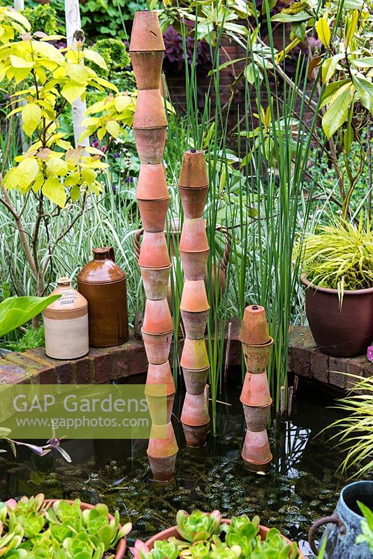 A small raised pond with stacked terracotta pots as a focal point.