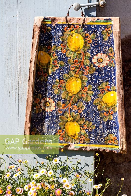 Tile painted with lemons and passionflowers on a door handle with Erigeron karvinskianus growing at its feet - Mexican fleabane - May, Herrenmühle Bleichheim