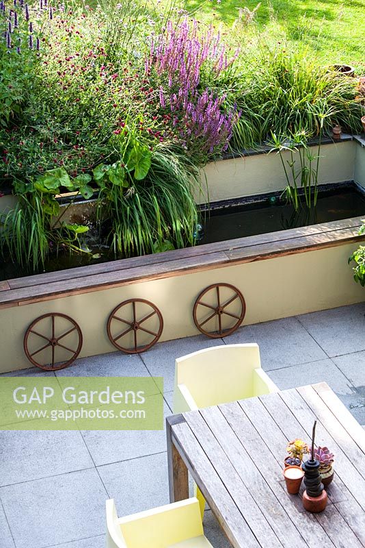 Above view of patio garden showing summer border with water feature, rustic wheels, table and chairs