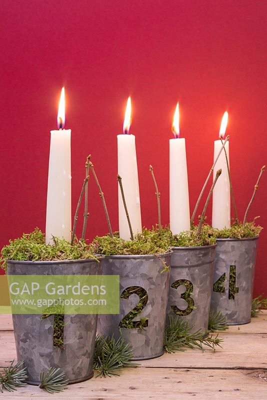Advent candles in numbered metal pots with moss, against a red background