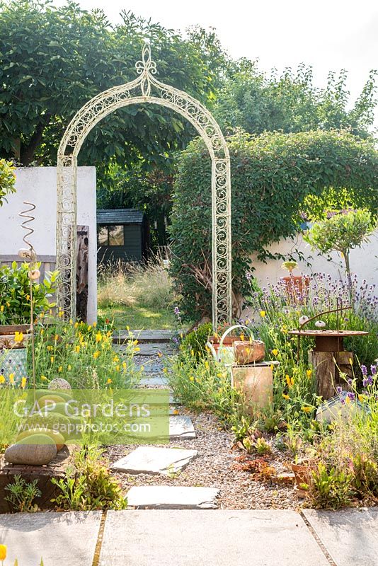 Courtyard garden with wirework arch, found objects, improvised sculptures and stepping stones leading to wild garden. Self seeded Eschscholzia californica.