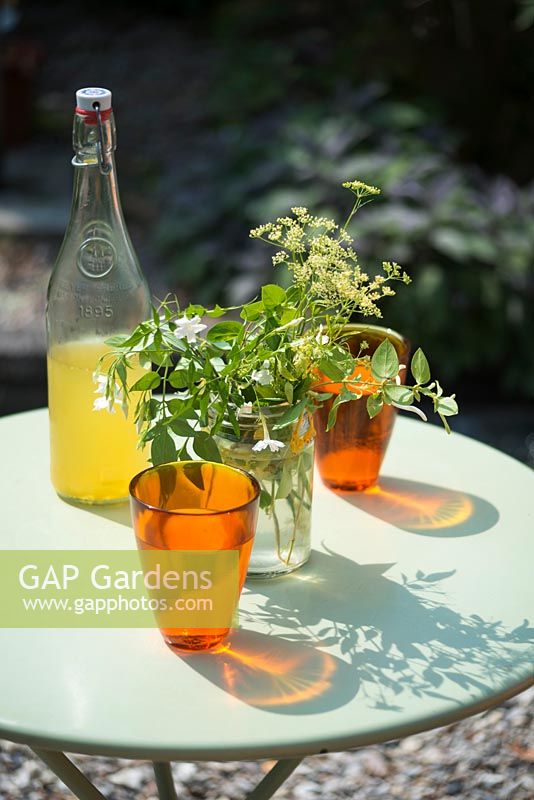 Orange glasses, bottle of cordial and flowers in jam jar on turquoise garden table