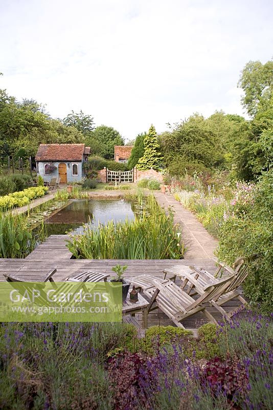 Natural Swimming Pool with wooden reclining chairs. Borders of rosmarinus officinalis and alchemilla mollis. Snares Hill Cottage, Essex
