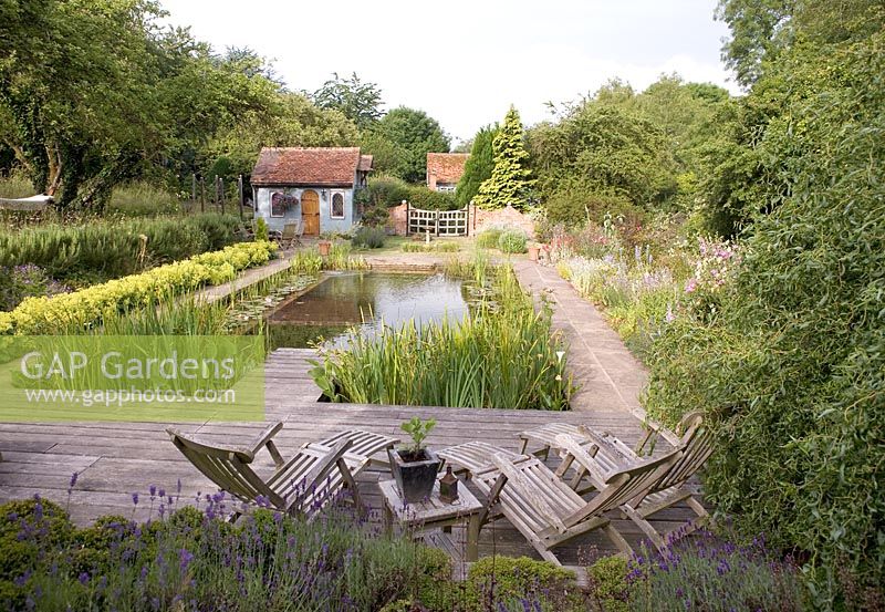 Natural Swimming Pool with wooden reclining chairs and borders of rosmarinus officinalis, alchemilla mollis. Snares Hill Cottage, Essex