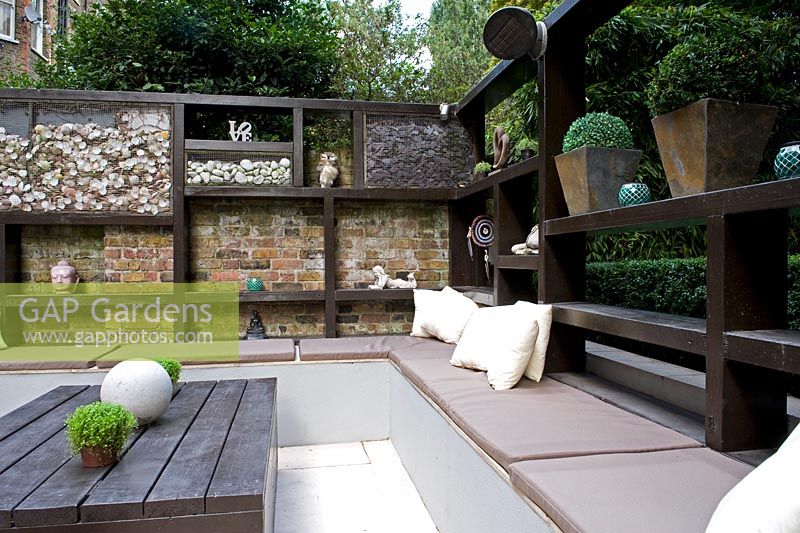 Geometric wooden seating area with cushions, ornaments and containers.

