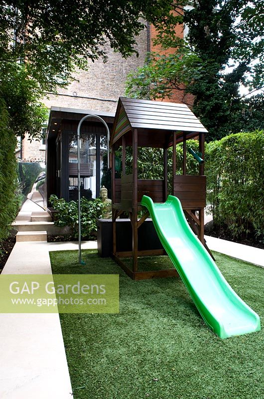 Children's play area with astroturf, slide and playhouse. Garden room building in background