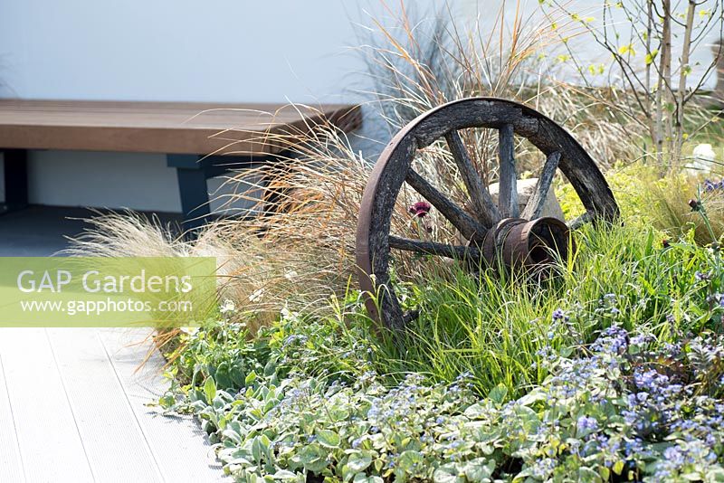 Old cart wheel with planting of  Stipa tenuissima, Anemone sylvestris, Brunnera macrophylla 'Jack Frost' - The Low Line, RHS Malvern Spring Festival 2016