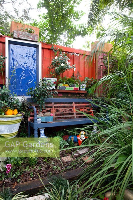 A painted garden bench in front of a collection of retro painted cement pots and a blue framed wall decoration.