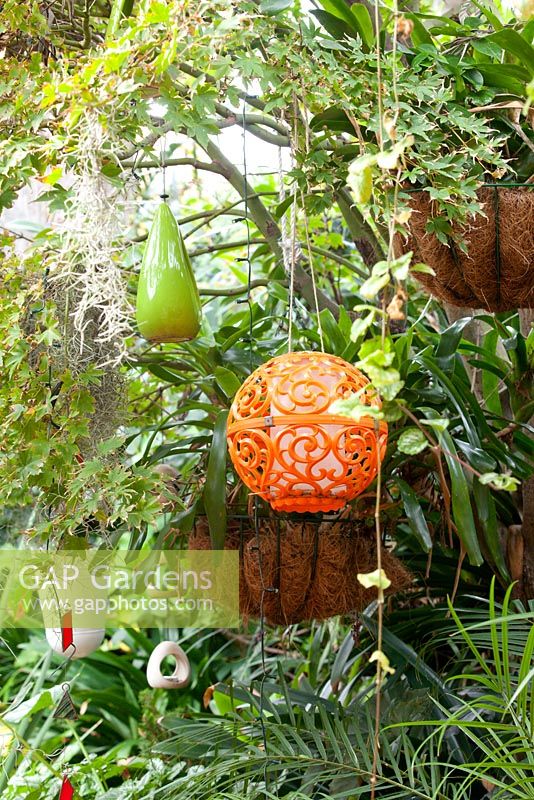A collection of quirky decorative objects hanging in a tree including a retro orange plastic globe and a green glazed ceramic bottle.