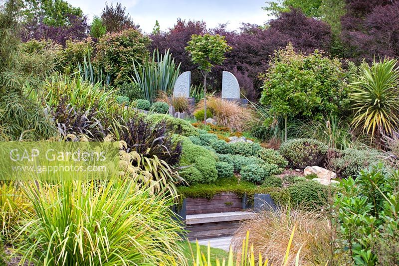 Selection of native Hebes, shrubs and grasses with antique statues at Bhudevi Estate garden, Marlborough, New Zealand.