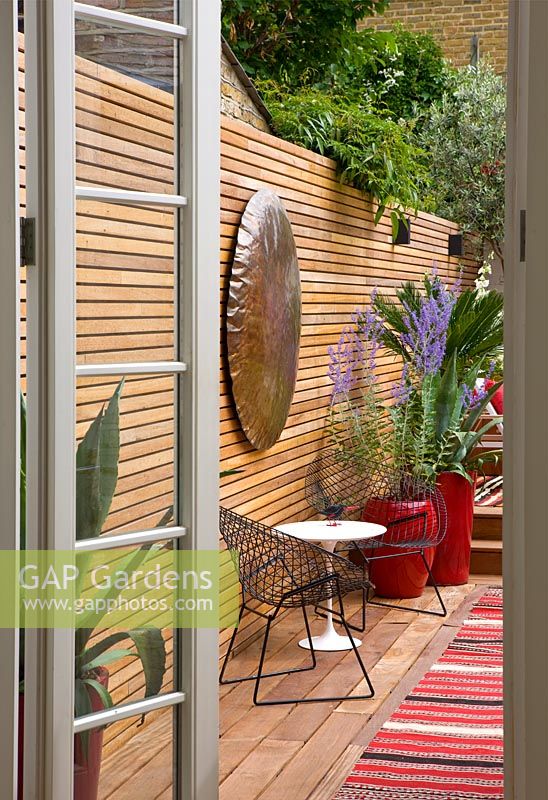 Brazilian hardwood decking with red containers planted with agave, perovskia and a fern, copper disc on fence. Ben De Lisi House and Garden, London