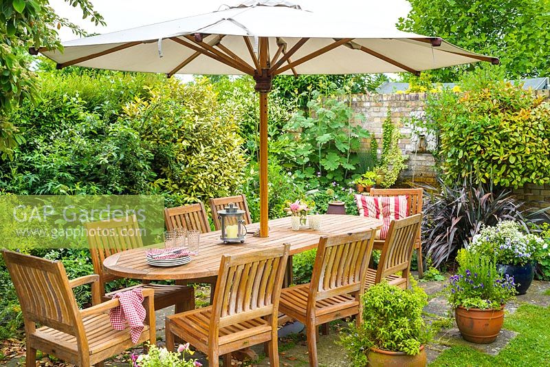 Outdoor dining area in secluded corner of family garden with wooden table, chairs and parasol.