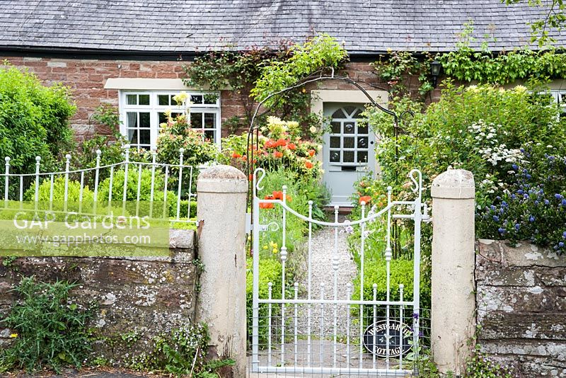 Simple metal gate and stone wall surrounds the garden at West Garth Cottage with box edged beds inside.