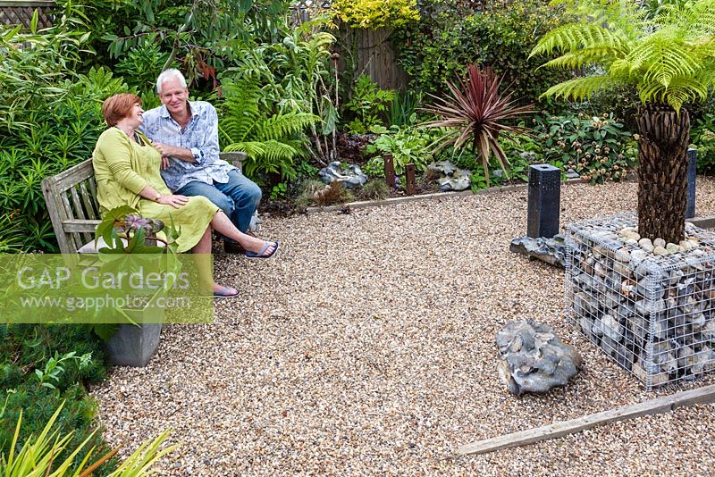 Bill and Bev Kerr in the most recently developed part of their garden. Planting includes Euphorbia mellifera, variegated bamboo, Dicksonia antarctica and castor oil plant - Ricinus communis in a galvanised metal container.