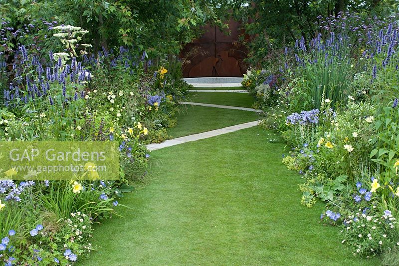 The Dog's Trust:' A Dog's Life', designed by Paul Hervey-Brookes. A stretch of lawn, criss-crossed by zig-zag paving. Plants include verbena bonariensis, agastache, angelica, cosmos, blue campanulas and geraniums and hemerocallis, with alchemilla mollis and erigeron karvinskianus. Hampton Court Flower Show July 2016