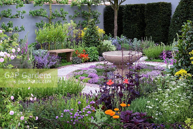The St John's Hospice Garden, The Modern Apothecary. Oak bench and water basin in herb garden with circular cobble stone path. RHS Chelsea Flower Show 2016 - Designer: Jekka McVicar, Sponsor: St John's Hospice
