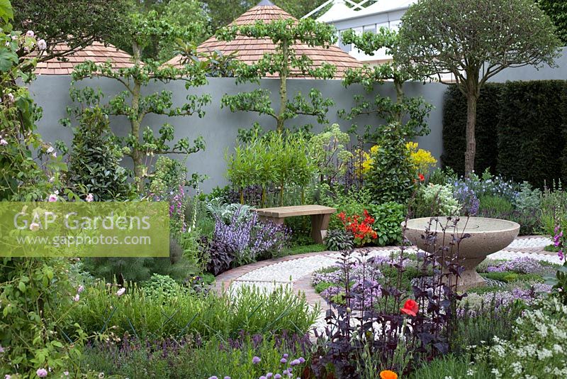 The St John's Hospice - A Modern Apothecary, inspired by the healing power of plants and a quote from Hippocrates 'Let food be your medicine and medicine be your food', calming stone water feature in the centre of a spiral cobbled path, bordered by herbs such as fennel, bay, and lavender. RHS Chelsea Flower Show, 2016