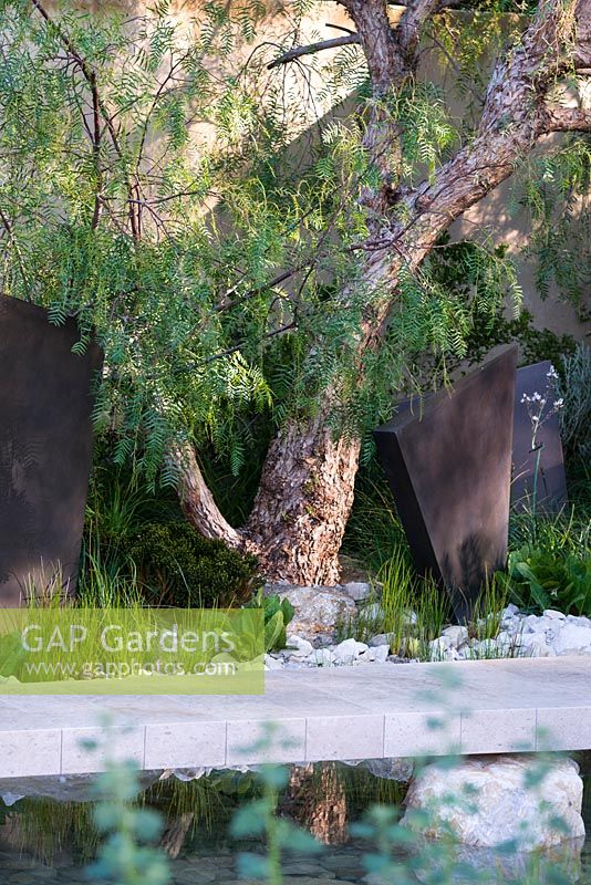 The Telegraph Garden, view of a tree - Schinus molle between geometric bronze sculptures. RHS Chelsea Flower Show 2016. Designer: Andy Sturgeon - Sponsor: The Telegraph