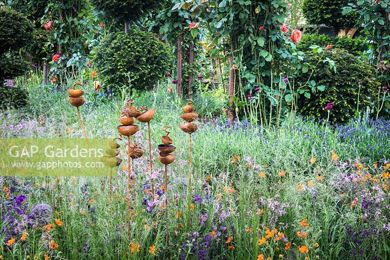 Rusted sculptural bird feeders in the perennial meadow with grasses, allium, geum, ragged robin, Aquilegia 'Blue Barlow' and Lysimachia 'Beaujolais' in the RHS Greening Grey Britain for Health, Happiness and Horticulture Garden. RHS Chelsea Flower Show 2016 - Designer: Annie-Marie Powell