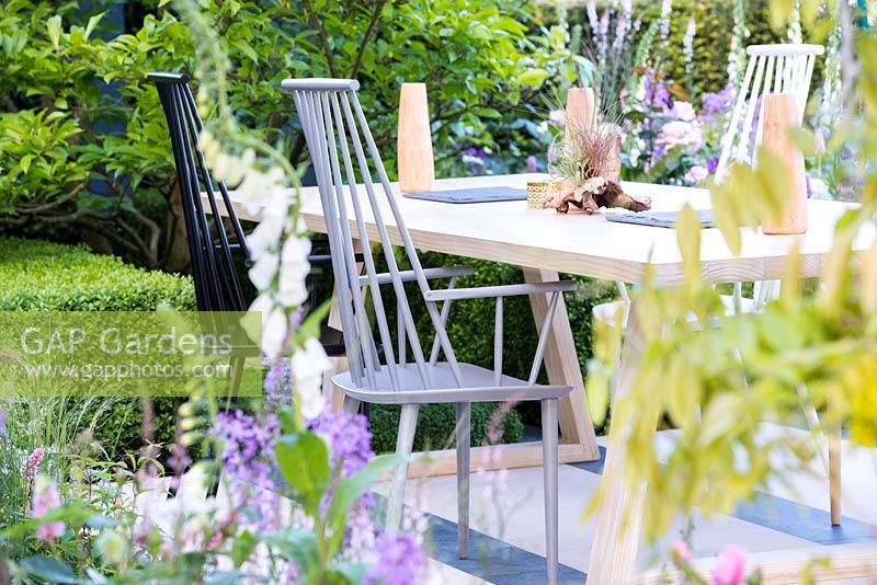 The LG Smart Garden, view of a patio with wooden chairs and table designed by Nils Verweij surrounded by spring flowers in pale colours. RHS Chelsea Flower Show 2016. Designer: Hay Young Hwang, Sponsors: LG Electronics