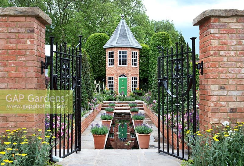 The Harrods British Eccentrics Garden. View through gates to the pool, house and borders. RHS Chelsea Flower Show 2016, Designer - Diarmuid Gavin.