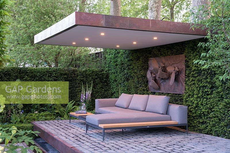 Covered outdoor seating area with lighting on a brick paved platform surrounded by Taxus baccata hedging   - The Husqvarna Garden presents 'Support, a garden in Melbourne', RHS Chelsea Flower Show 2016