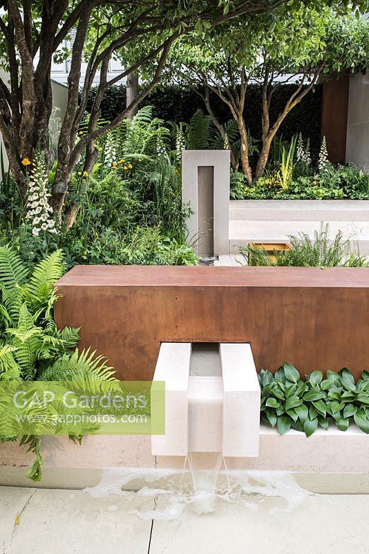 Garden of Mindful Living, view of limestone water feature and pool surrounded by  Digitalis 'Dalmatian White', Hosta 'Devon Green', Dryopteris erythrosora, Blechnum tabulare, beneath multi-stemmed trees. RHS Chelsea Flower Show 2016, Design: Paul Martin, Sponsor: Vestra Wealth LLP