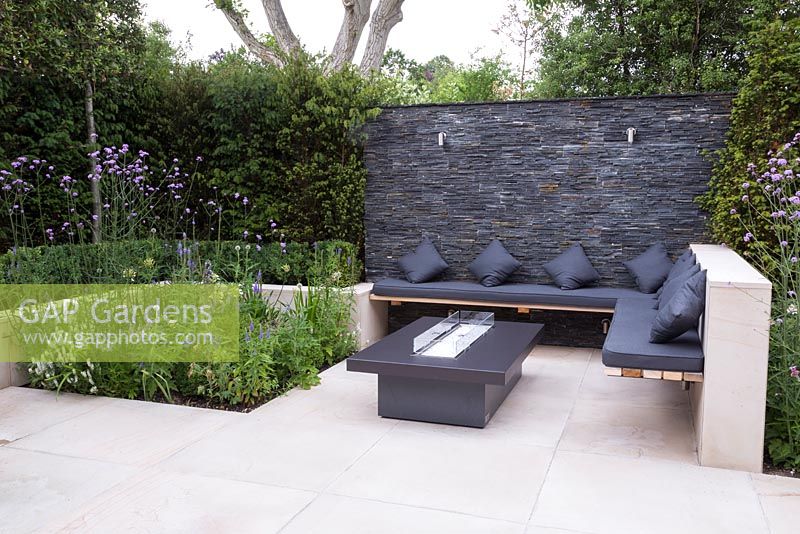 Overview of sandstone patio with a secluded seating area and dry stone slate wall. Featuring sunken planting of Verbena bonariensis, Veronica and Agapanthus